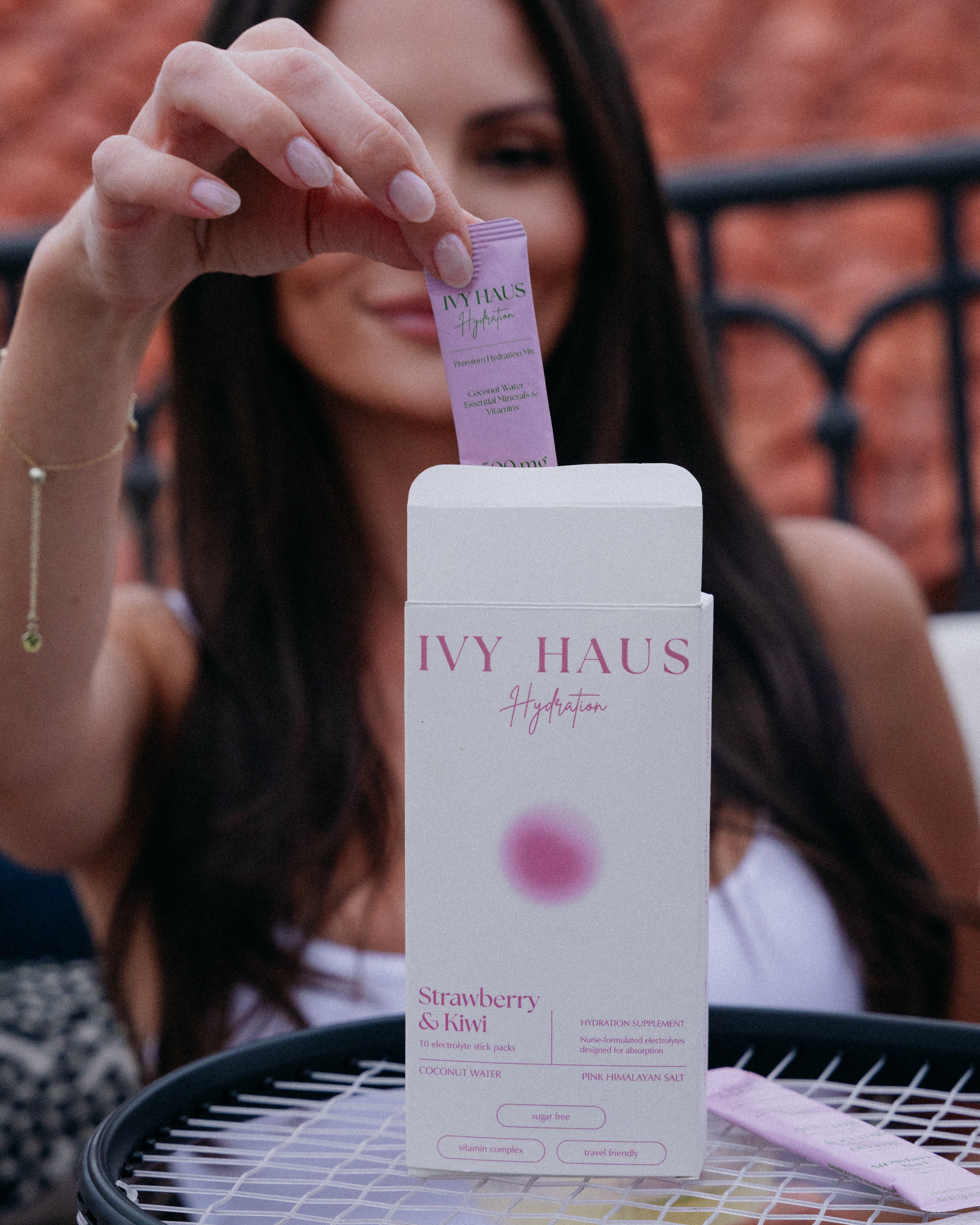 Girl pulling an Ivy Haus Strawberry Kiwi hydration mix packet out of the box